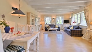A spacious living room with a dining area, featuring a wooden table, chairs, a sofa set, and a television. - Landhaus Vilmnitz - Wohnung 9 - Landhaus Vilmnitz, Wohnung 9 (Putbus)