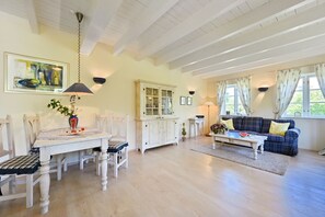 Ein geräumiges Wohnzimmer mit Essbereich, Holzböden und einem großen Fenster mit Vorhängen.