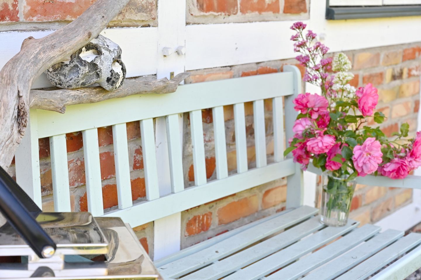 A bench with a white picket design, a vase with pink flowers, and a rustic branch.