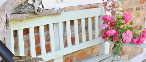 A bench with a white picket design, a vase with pink flowers, and a rustic branch.