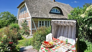 A traditional house with a thatched roof, a brick exterior, and a garden with flowers and a table set for a meal. - Landhaus Vilmnitz - Wohnung 9 - Landhaus Vilmnitz, Wohnung 9 (Putbus)