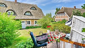 Een traditioneel huis met rieten dak, een tuin met een eettafel en een rieten stoel.