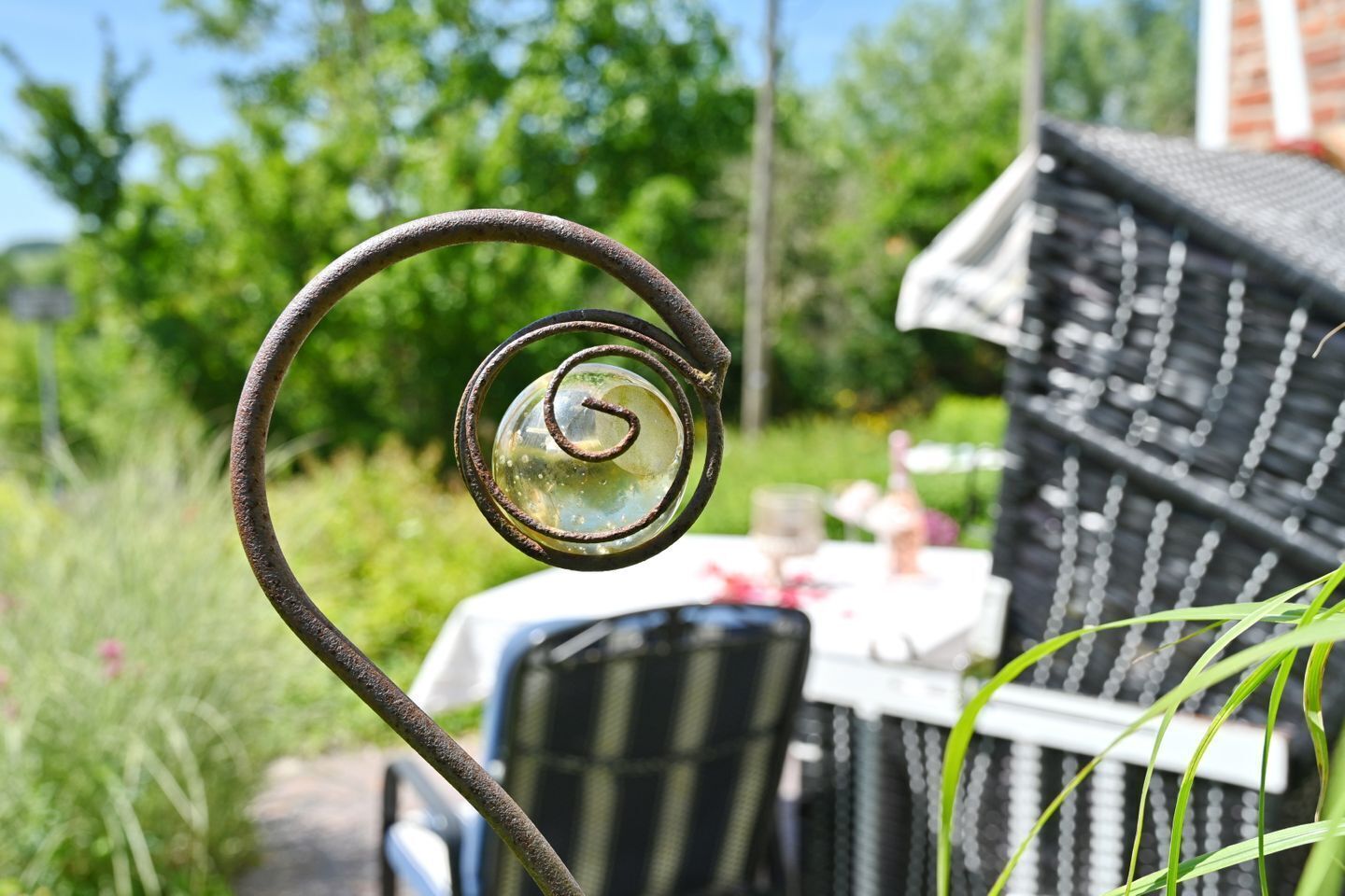 A garden with a metal spiral structure, a table with chairs, and a building in the background.