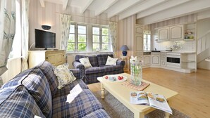 Een ruime woonkamer met een zithoek, een eettafel met een tijdschrift, en een keuken met kasten en een fornuis.