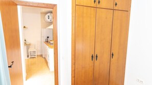 Una habitación con un armario de madera, un lavamanos blanco y una pequeña cocina con una silla y un refrigerador.
