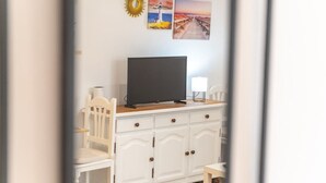Una habitación con un armario blanco, un televisor encima y una silla.