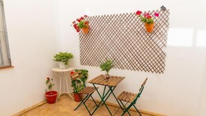 Un pequeño patio con mesa de madera y dos sillas, rodeado de plantas en macetas y un cerramiento de celosía.