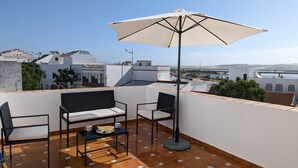 A rooftop terrace with a table, two chairs, and a large umbrella.