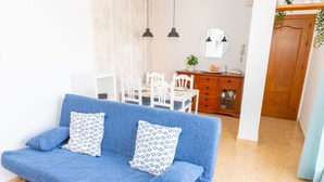 A blue sofa with patterned cushions, a dining table with chairs, a wooden cabinet, and a mirror on the wall.