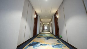 A long, narrow hallway with a patterned carpet, white walls, and wooden doors on both sides.