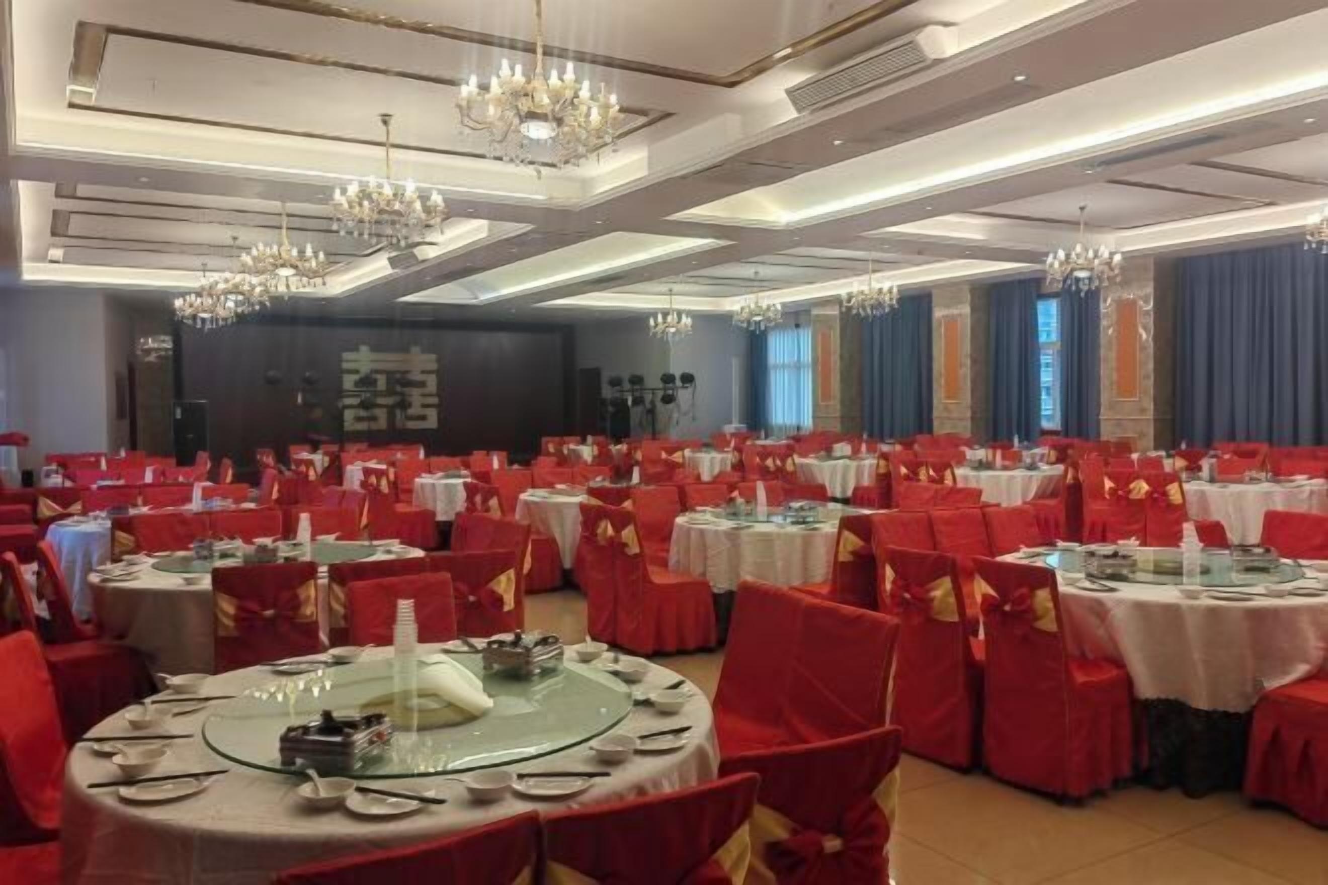 A banquet hall with round tables, red chairs, and chandeliers.