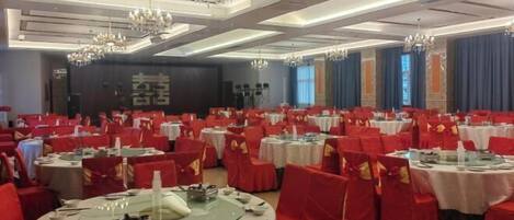 A banquet hall with round tables, red chairs, and chandeliers.