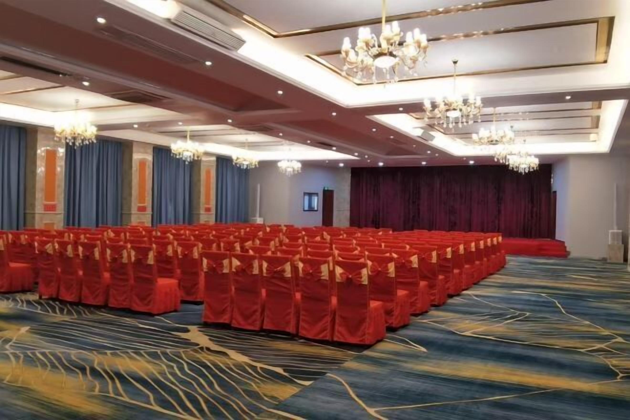 A large conference room with rows of red chairs, a stage, and chandeliers.