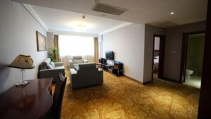 A hotel room with a living area featuring a sofa set, a TV, and a dining table.