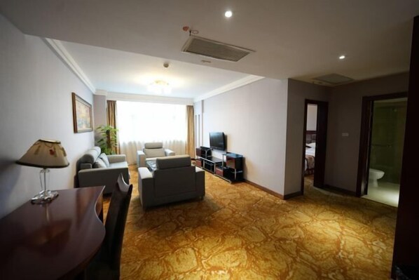 A hotel room with a living area featuring a sofa set, a TV, and a dining table. - Quanjun Hotel (Dawu)