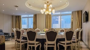 A dining area with a round table, six chairs, a chandelier, and large windows with curtains.