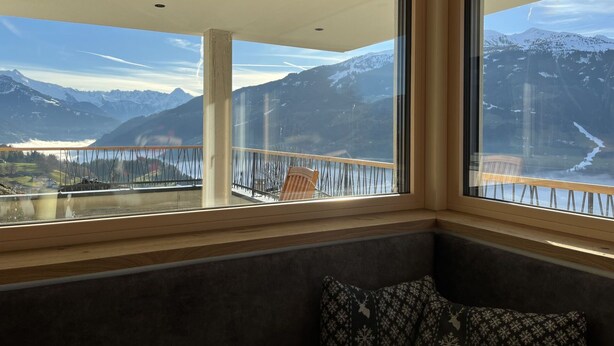 A room with a large window offering a view of snow-capped mountains and a lake. - Lovely apartment for 4 guests with WIFI, TV and panoramic view (Stumm)
