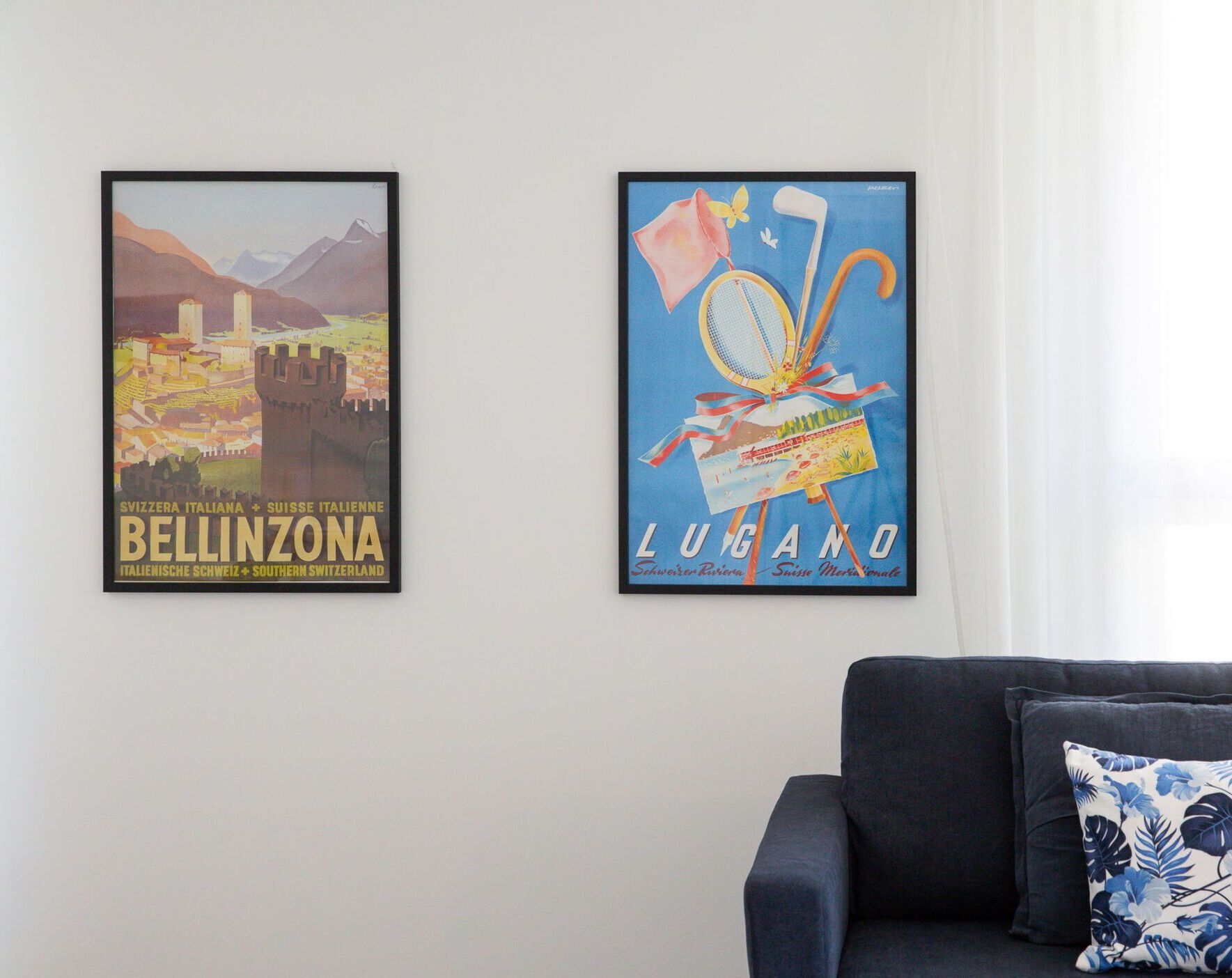 Two framed travel posters on a wall above a dark sofa.
