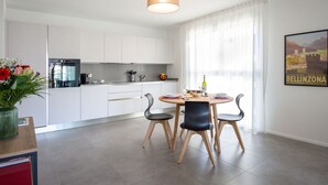 A modern kitchen with white cabinets, a built-in oven, and a dining area with a round table and four chairs.