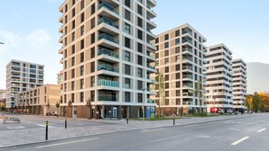 Un immeuble résidentiel moderne à plusieurs étages, doté de balcons, d’une façade sobre et surplombant un ciel dégagé.