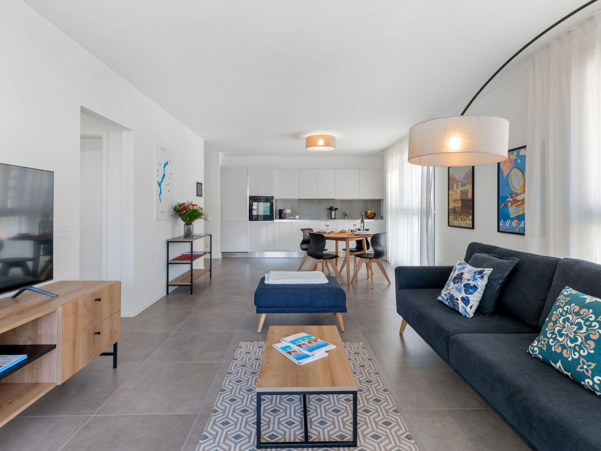 A modern living room with a TV, sofa, coffee table, and a dining area with chairs and a table.