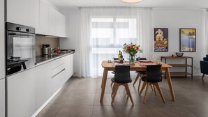 A modern kitchen with white cabinets, a built-in oven, and a dining area with a wooden table and chairs.