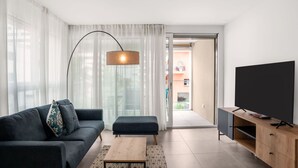 A modern living room with a dark sofa, a wooden coffee table, a large flat-screen TV, and a floor lamp.