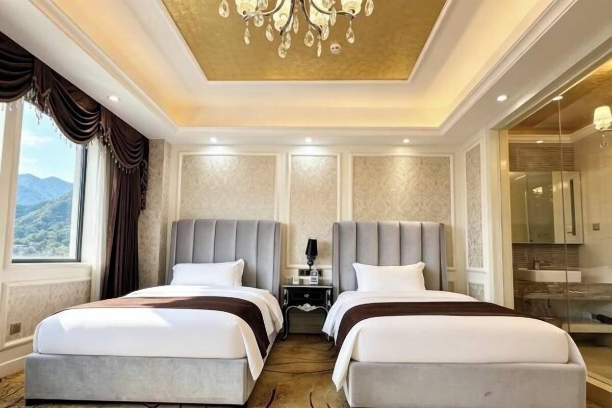 Ett hotellrum med två sängar, en kristallkrona, ett nattduksbord och utsikt över bergen.