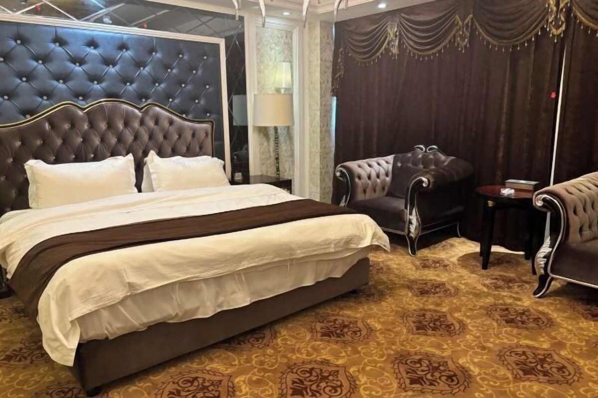 A large bed with a tufted headboard, a dark brown upholstered armchair, and a matching armchair.