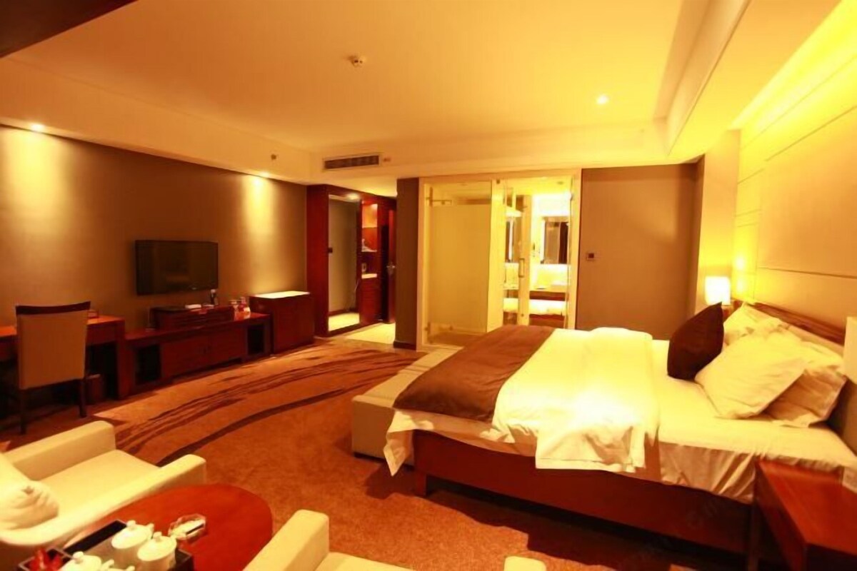 A hotel room with a bed, a TV, a desk, and a bathroom visible through an open door.
