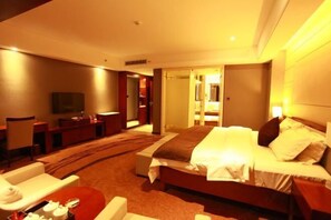 Ein Hotelzimmer mit Bett, Fernseher, Schreibtisch und einem durchgegangenen Tür erkennbaren Badezimmer.