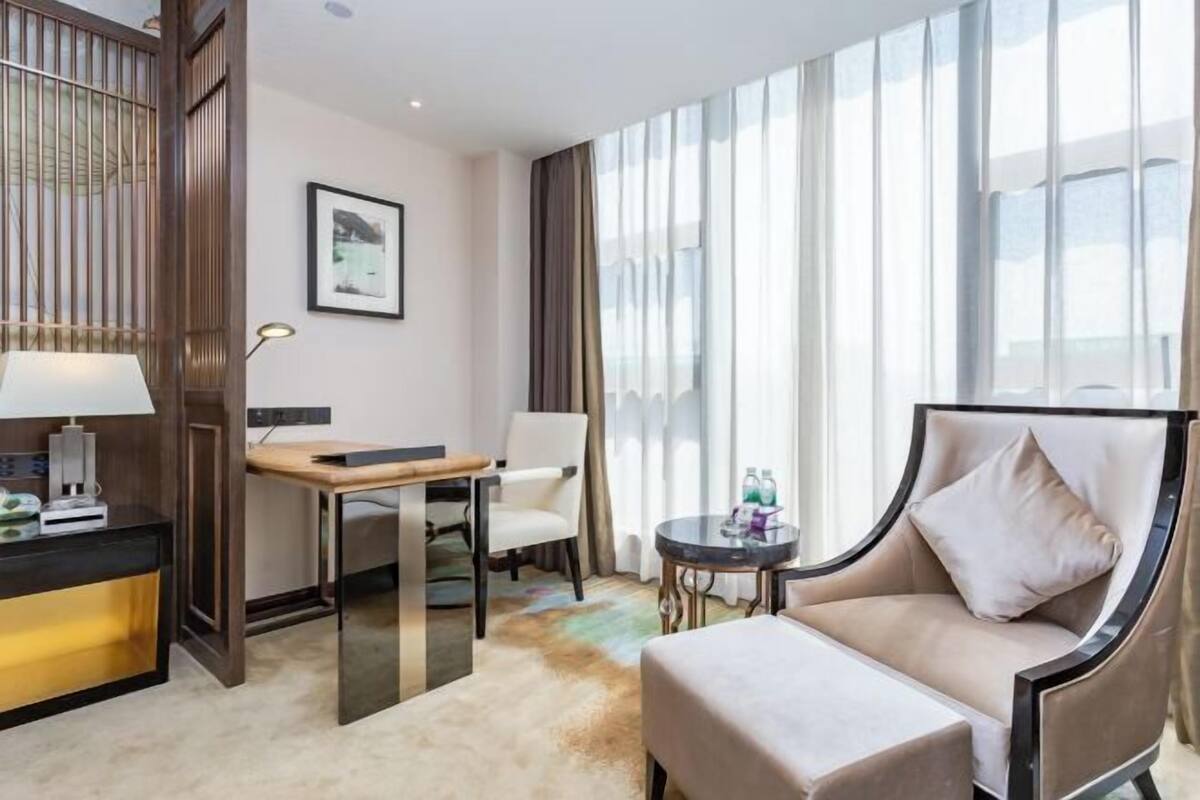 Une chambre d’hôtel avec un canapé, une petite table, un bureau, une chaise et une grande fenêtre avec des rideaux.