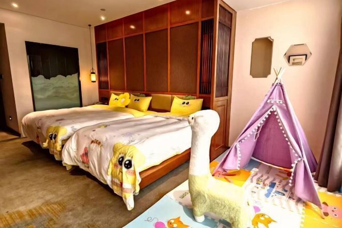 Une chambre avec un grand lit, une tête de lit en bois, une lampe fixée au mur et une petite structure ressemblant à une tente.