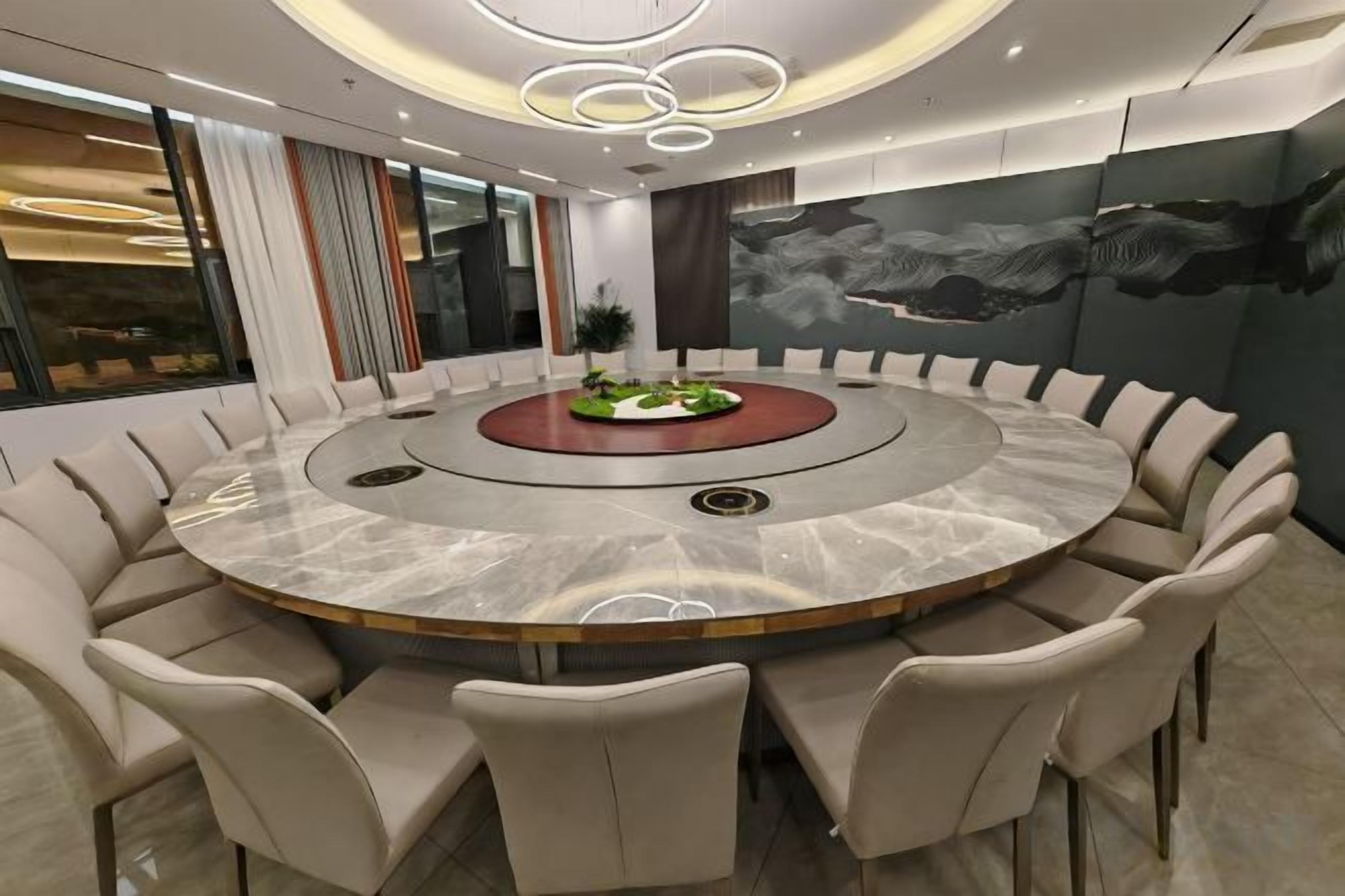 A modern conference room with a circular table, beige chairs, and a central plant.