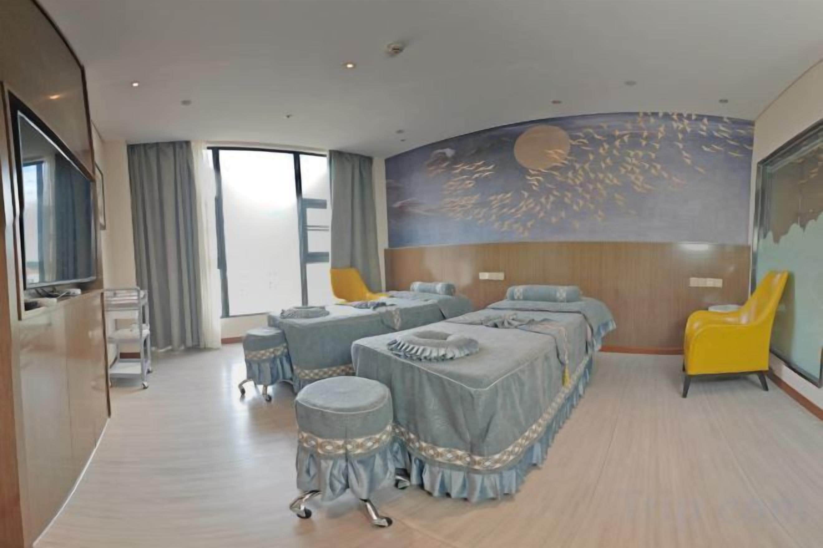 Une chambre d’hôtel avec un grand lit, un bureau et une chaise. Il y a une fenêtre avec des rideaux, une fresque murale et un téléviseur.