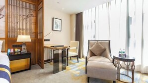 A hotel room with a bed, a desk with a lamp, a chair, a small round table, and a large window with curtains. - Qianshan Heyue Hotel (Suiyang)