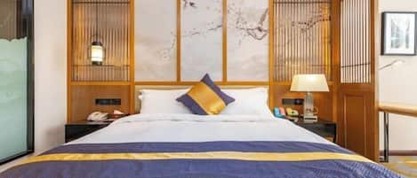 A hotel room with a large bed, wooden paneling, a nightstand with a lamp, and artwork on the wall.
