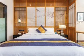 A hotel room with a large bed, wooden paneling, a nightstand with a lamp, and artwork on the wall. - Qianshan Heyue Hotel (Suiyang)