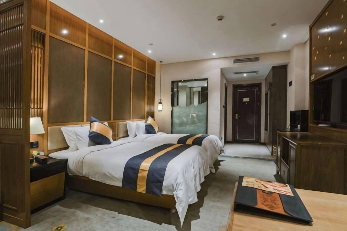 Une chambre d’hôtel avec deux lits, un bureau, une télévision et un mur recouvert de panneaux de bois.