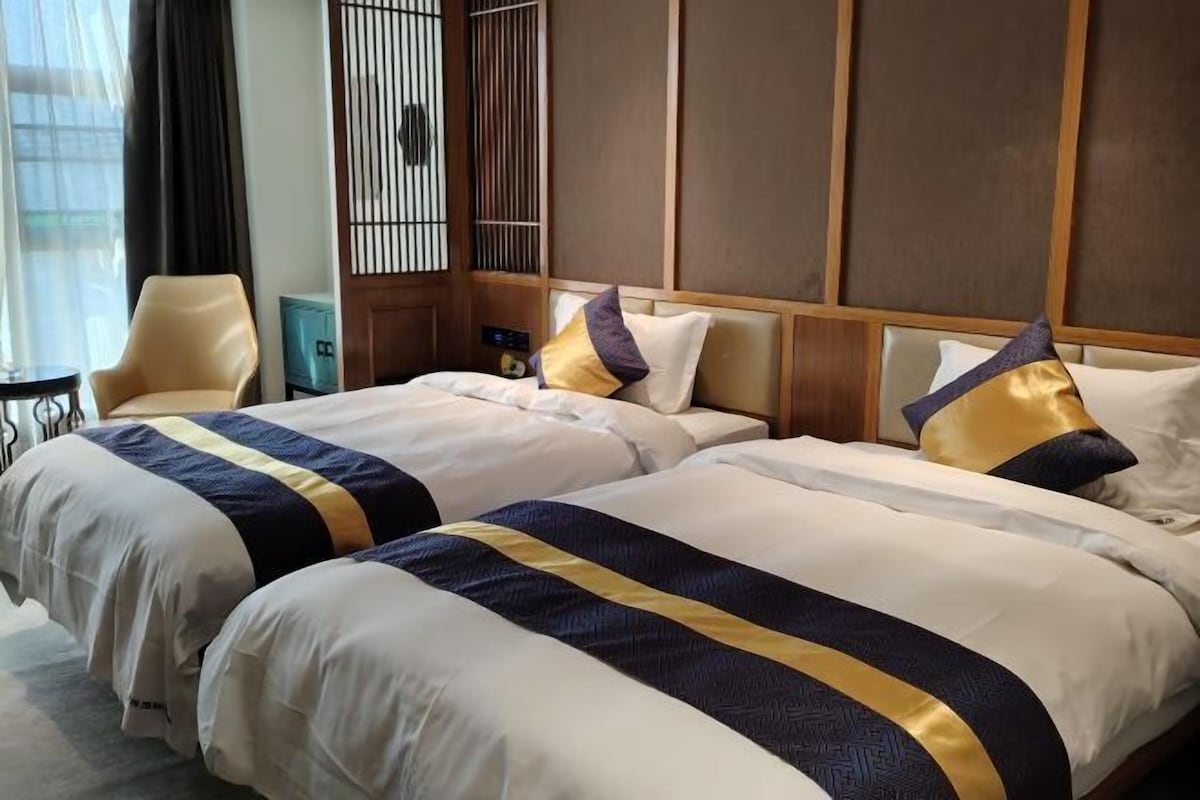 A hotel room with two beds, each with a white and navy blue striped bedspread, a wooden headboard, and a small table with a chair.