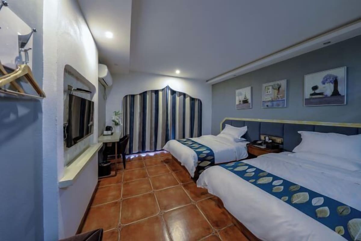 Habitación de hotel con dos camas, una ventana, una cortina, un escritorio y una pared con cuadros.