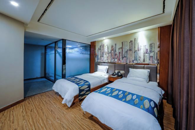 A hotel room with two beds, a cityscape mural, and a glass partition.