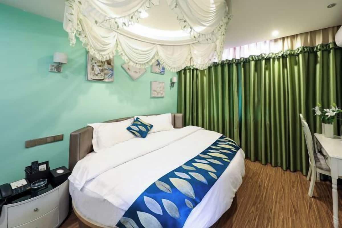 Habitación de hotel con cama, mesita de noche, escritorio y cortina verde.