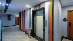 En hotelgang med moderne design, der inkluderer en central elevator, brandslukkere og en dør med skilt.