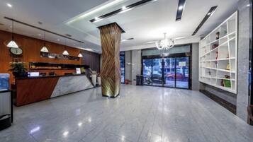 A hotel lobby with a reception desk, a large pillar, and a view of the outside.