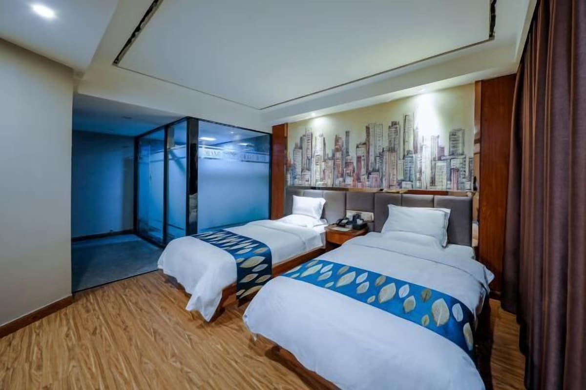 Habitación de hotel con dos camas, un mural con vista a la ciudad en la pared y piso de madera.