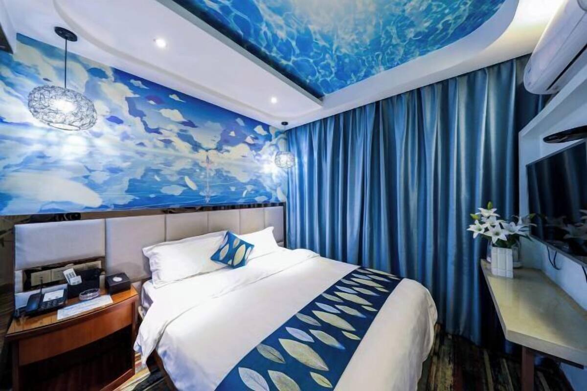 Una habitación de hotel con una cama, una mesita de noche, un escritorio, una silla, una pared con un diseño abstracto azul y una cortina.