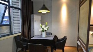 Et værelse med spisebord, stole, en vase med blomster, en loftslampe og en seng med gavl.