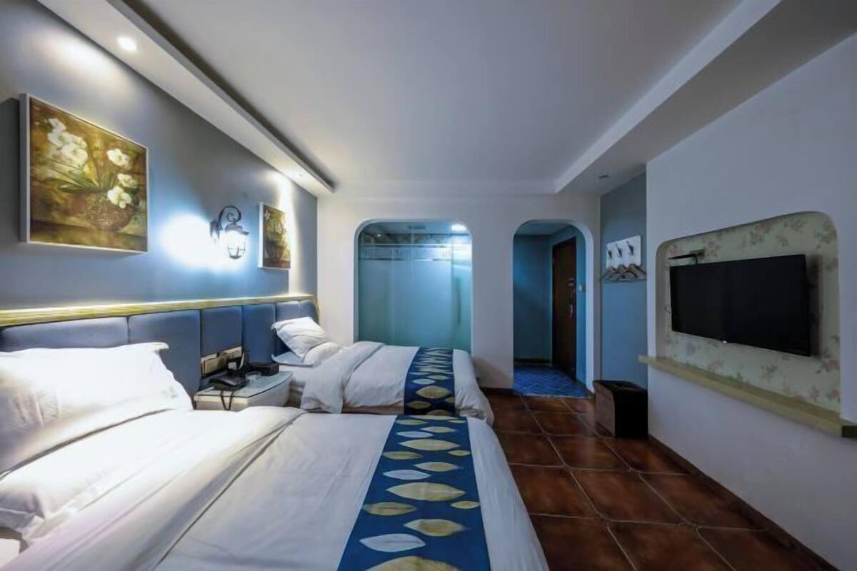 Habitación de hotel con dos camas, televisión, obras de arte en las paredes y un baño visible a través de un arco.
