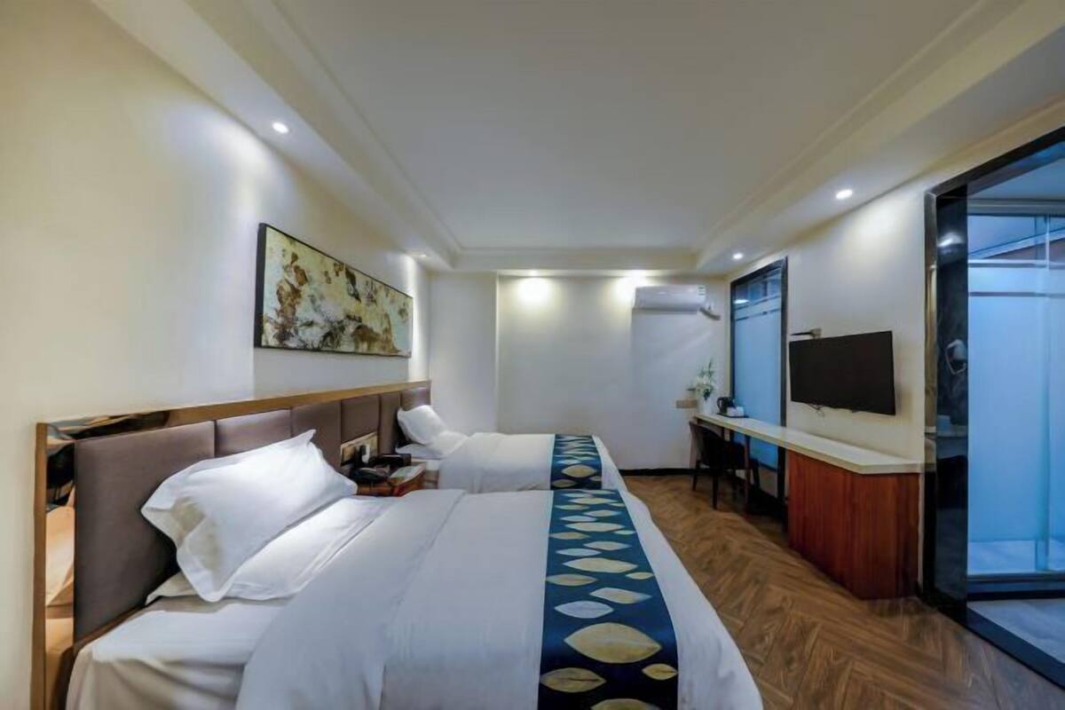Habitación de hotel con dos camas, un escritorio, un televisor y un ventanal grande.